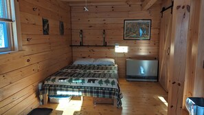 A wooden cabin room with a bed, a TV, and a window.