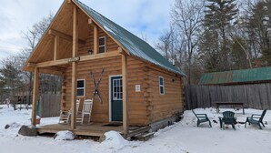 A wooden cabin with a porch, a green door, and skis leaning against the wall.