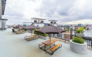 Eine Dachterrasse mit Picknicktischen und Sonnenschirmen mit Blick auf eine Stadtlandschaft.