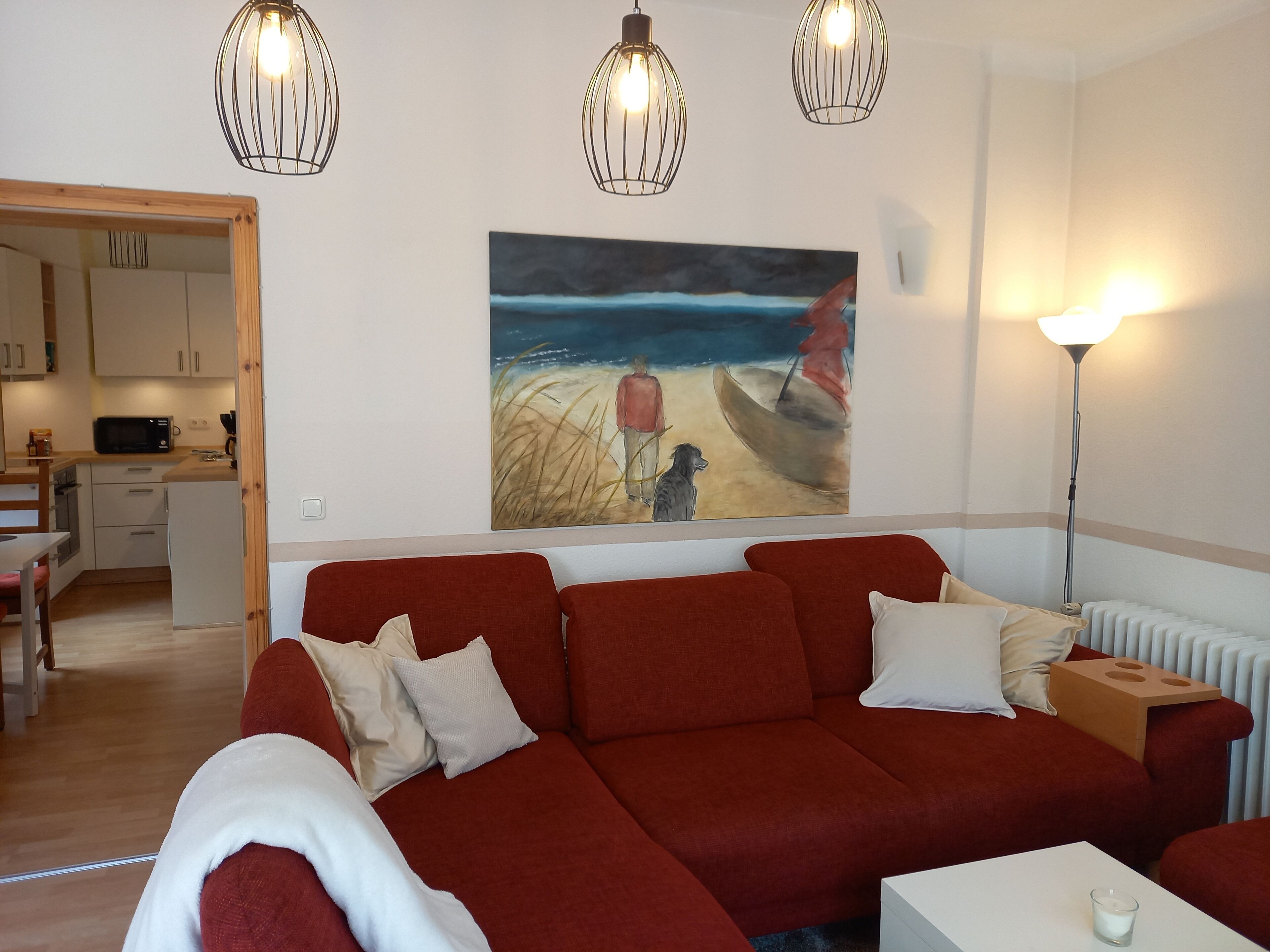 A living room with a red sofa, a painting of a beach scene, and a white radiator.