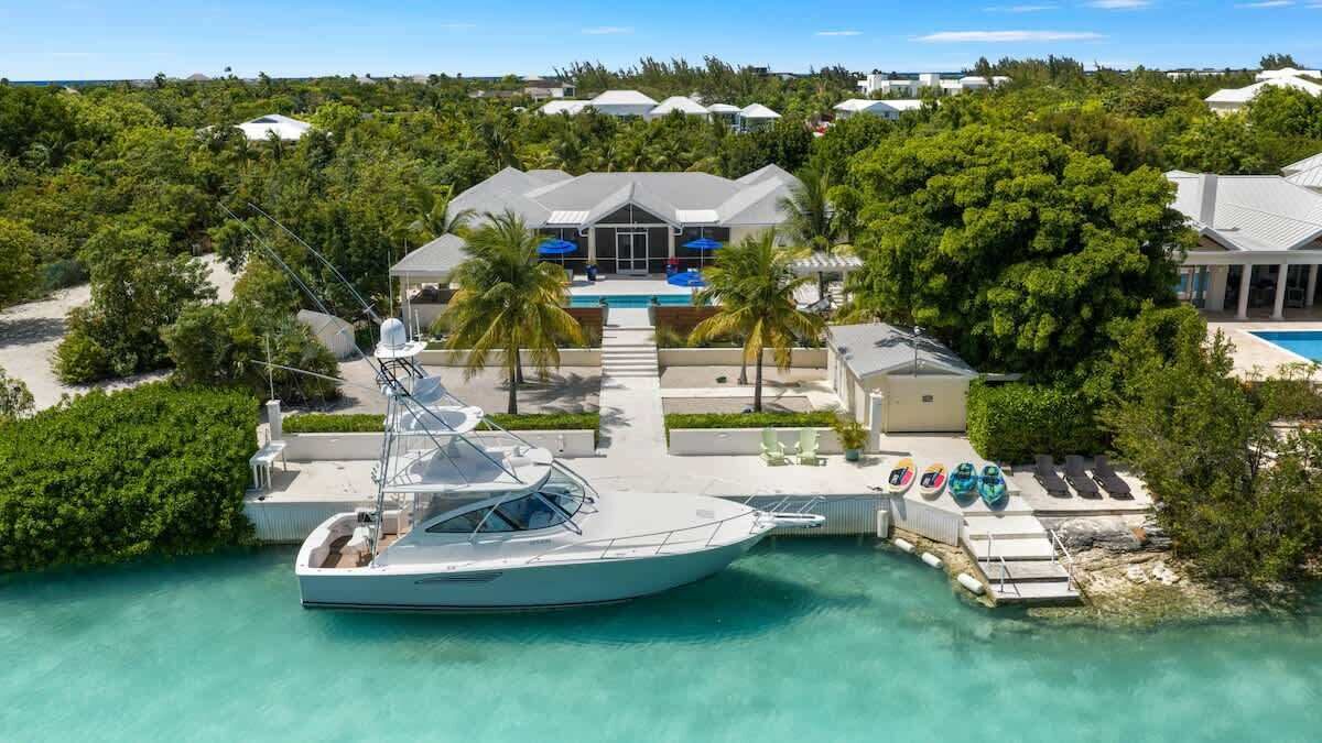 A yacht docked at a resort with a pool, palm trees, and a view of the surrounding landscape.