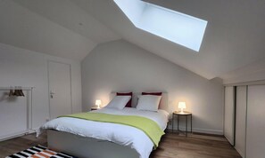 A bedroom with a skylight, a bed with white and green bedding, two bedside lamps, and a wooden floor. - La Nichée Cosy House to Share (Bazancourt)