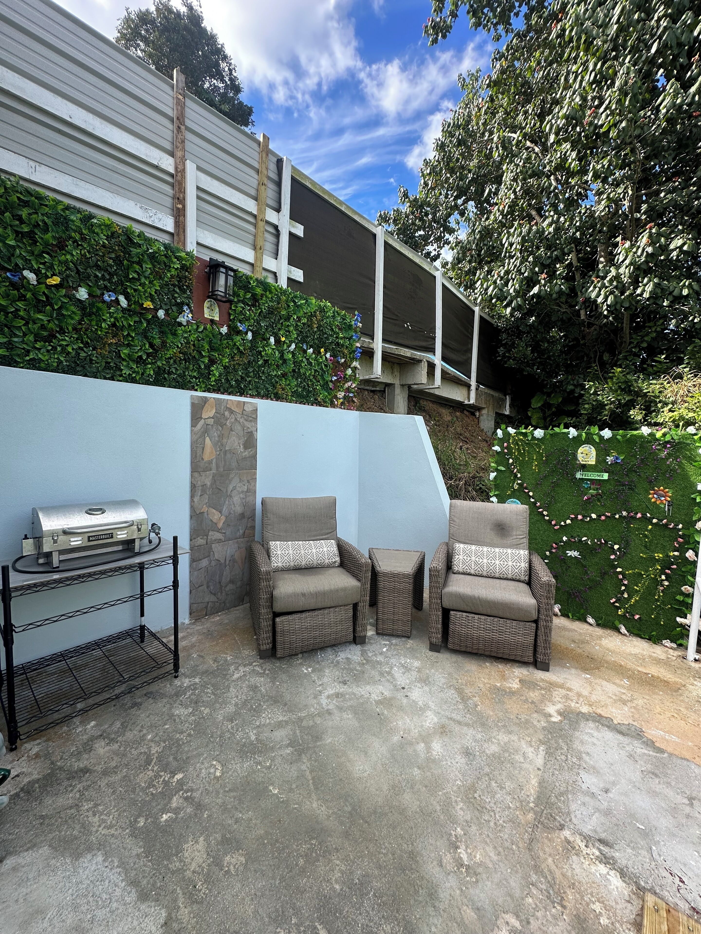 Une terrasse extérieure avec deux fauteuils en osier et un barbecue.