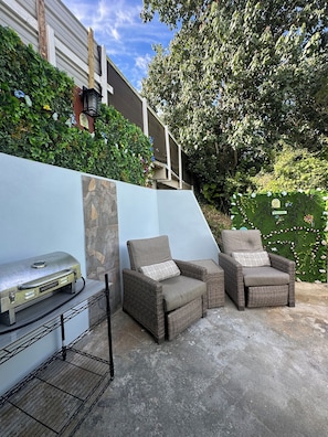 Un patio al aire libre con una parrilla, dos sillas de mimbre y una pared de piedra.