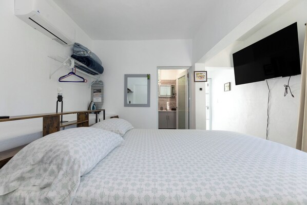 A bedroom with a bed, a TV mounted on the wall, a mirror, and a door leading to a bathroom.