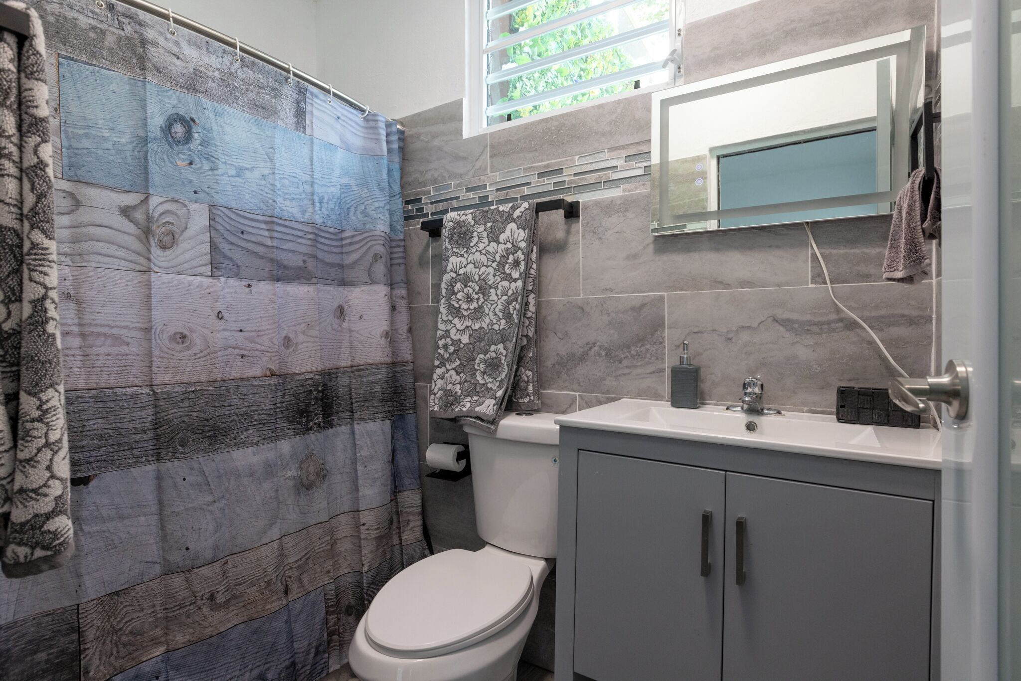 Une salle de bain avec un rideau de douche fait d’un matériau qui ressemble au bois, des toilettes, un lavabo avec un miroir au-dessus et une serviette accrochée au mur.