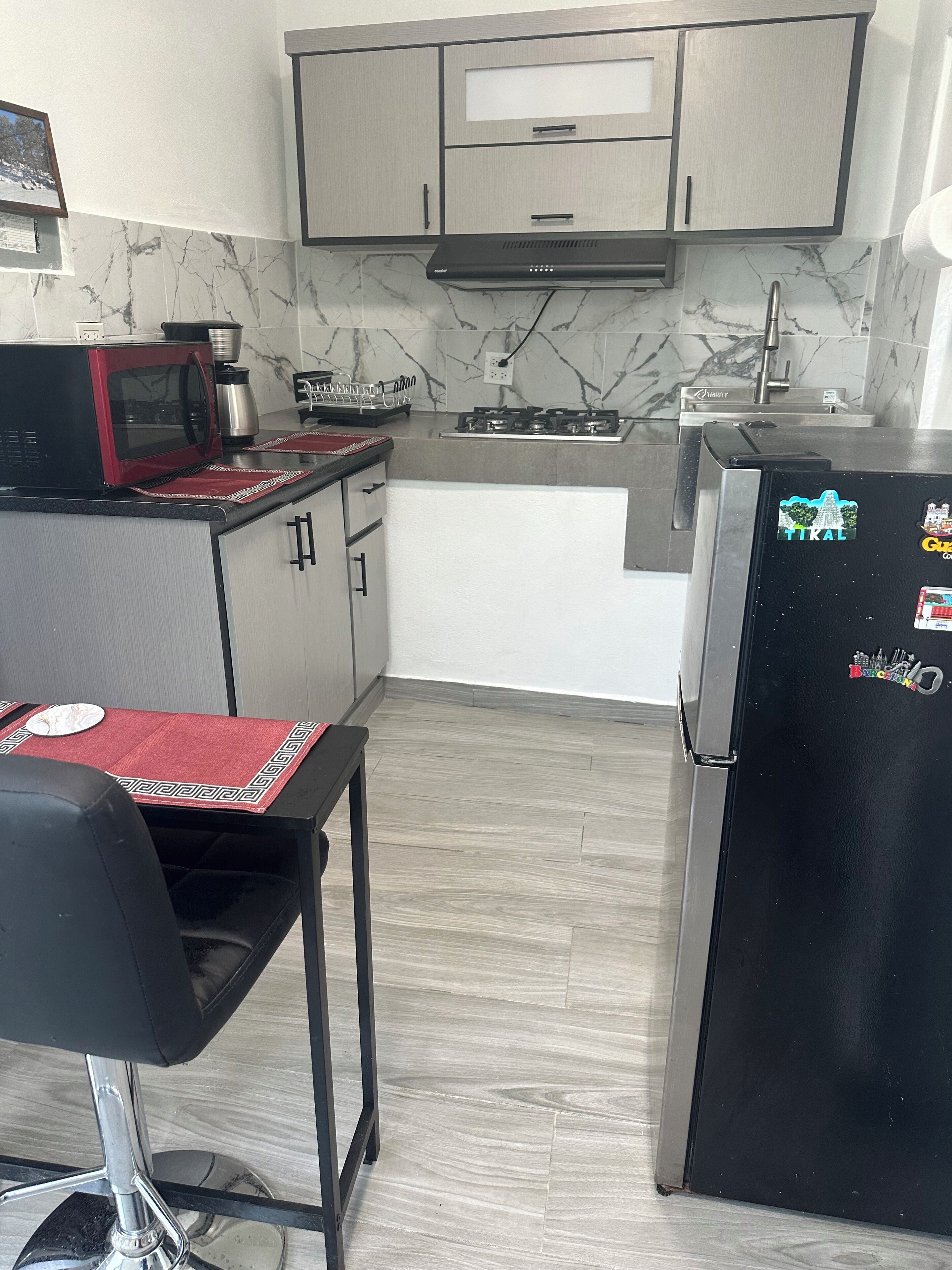 A compact kitchen with a microwave, stove, and refrigerator. There is a small dining table with a chair.