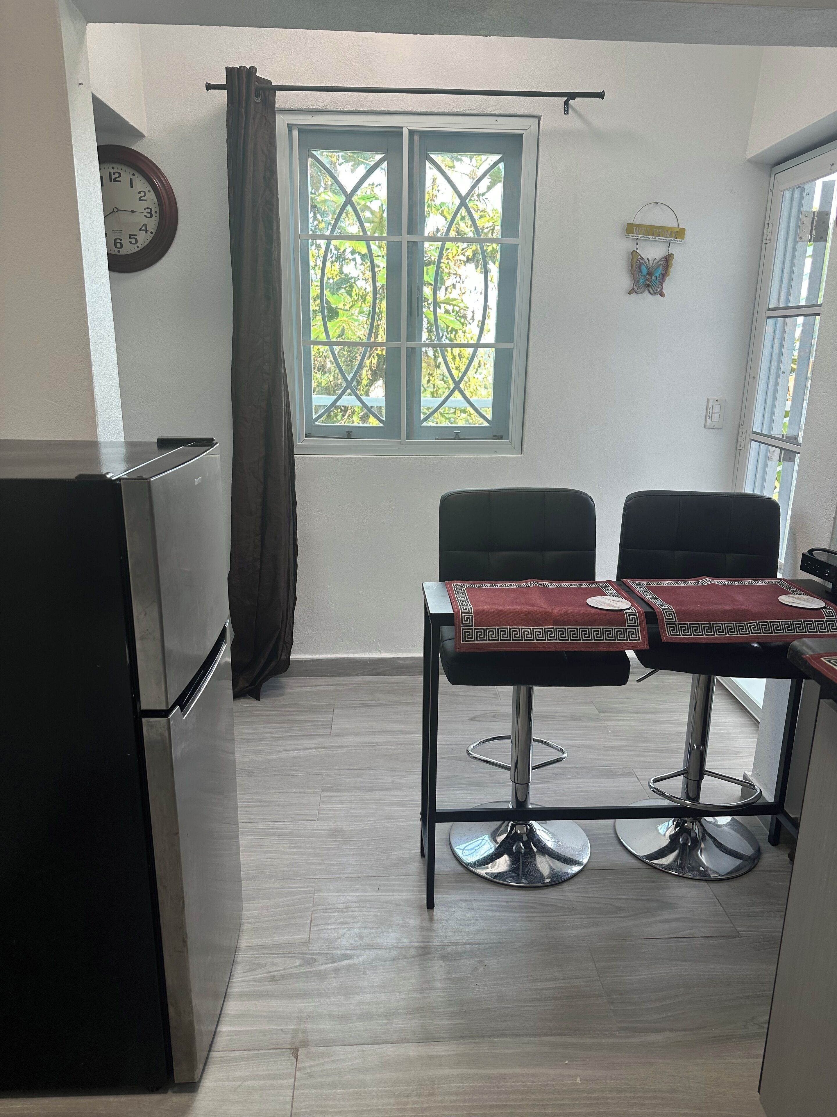 A compact kitchen with a refrigerator, a window with a curtain, and a dining area with two chairs and a table.