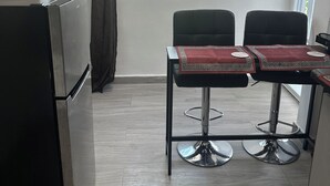 Una cocina compacta con refrigerador, ventana con cortina y comedor con dos sillas y una mesa.