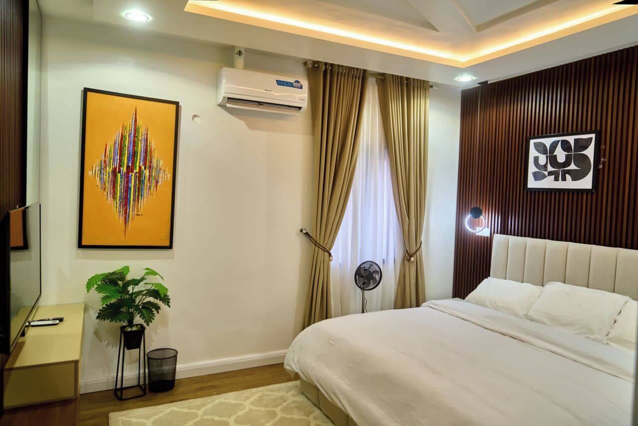 Un dormitorio moderno con cama, aire acondicionado, cortinas, ventilador y una obra de arte enmarcada en la pared.