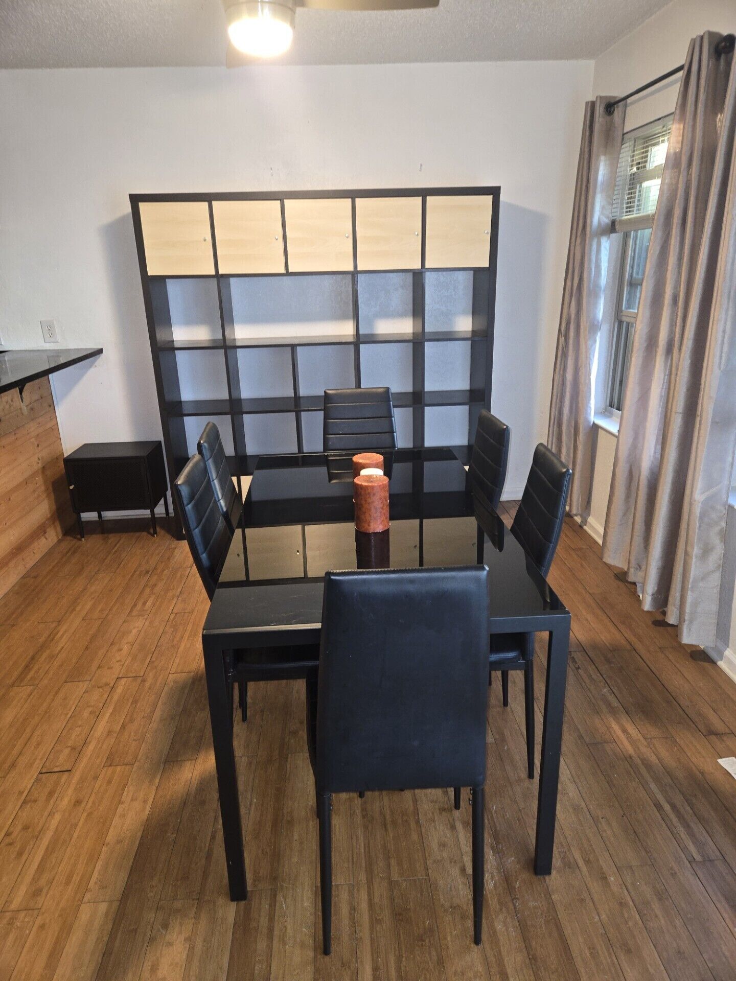 A dining area with a black table and chairs, a wooden partition, and a window with curtains.