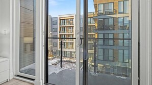 Ein modernes Apartment mit großen Fenstern, Blick auf benachbarte Gebäude und einem sichtbaren Balkon.