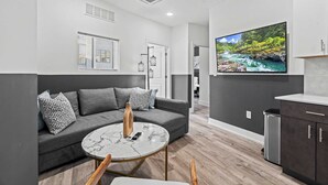 Ein modernes Wohnzimmer mit einem grauen Sofa, einem Marmortisch und einem Fernseher, der eine Flusslandschaft zeigt.