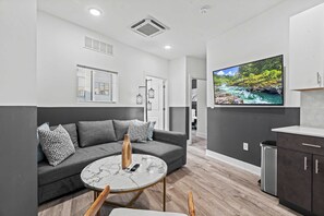 Ett modernt vardagsrum med en grå soffa, ett soffbord i marmor och en tv-skärm som visar ett landskap med en flod.