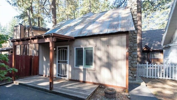 Eine kleine Holzhütte mit einem Metalldach, einer Veranda und einem weißen Zaun.