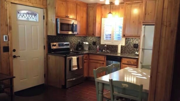 A kitchen with wooden cabinets, a microwave, a stove, and a dining table with chairs. - Romantic one bedroom, one bath cabin with white picket fence in.
Extremely cozy. (South Lake Tahoe)