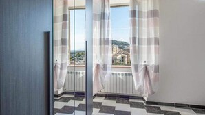 Ein Zimmer mit großem Fenster, Schachbrettfußboden und Blick auf eine Stadtlandschaft.