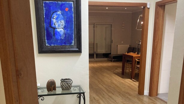 Een gang met houten vloer, een glazen consoles en decoratieve objecten, en een schilderij in een lijst aan de muur.