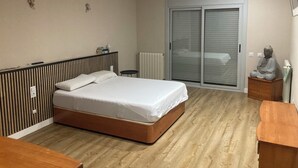 Een slaapkamer met een bed, een houten dressoir, een beeld en een schuifdeur met glas.