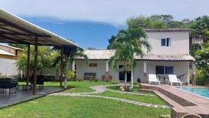 Un patio techado con mobiliario exterior, una piscina y un césped cuidado.