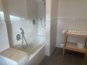 A bathroom with a bathtub, shower, and a shelf with toiletries. - Vacation room on the pony farm with self-catering (Lingen)