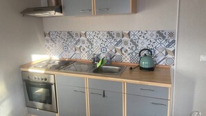 Cozinha compacta com fogão, forno e pia, bancada de madeira e painel decorativo.