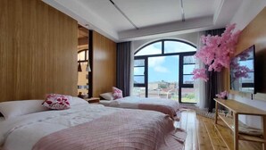 Ein Hotelzimmer mit zwei Betten, Holzboden, großen Fenstern und Blick auf die Stadt.