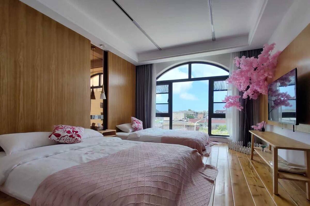 Habitación de hotel con dos camas, suelo de madera, ventanas amplias y vista a la ciudad.