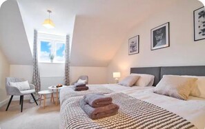 A bedroom with a bed, two chairs, a small table, and a window with curtains. - Modern Townhouse in Peterborough (Peterborough)
