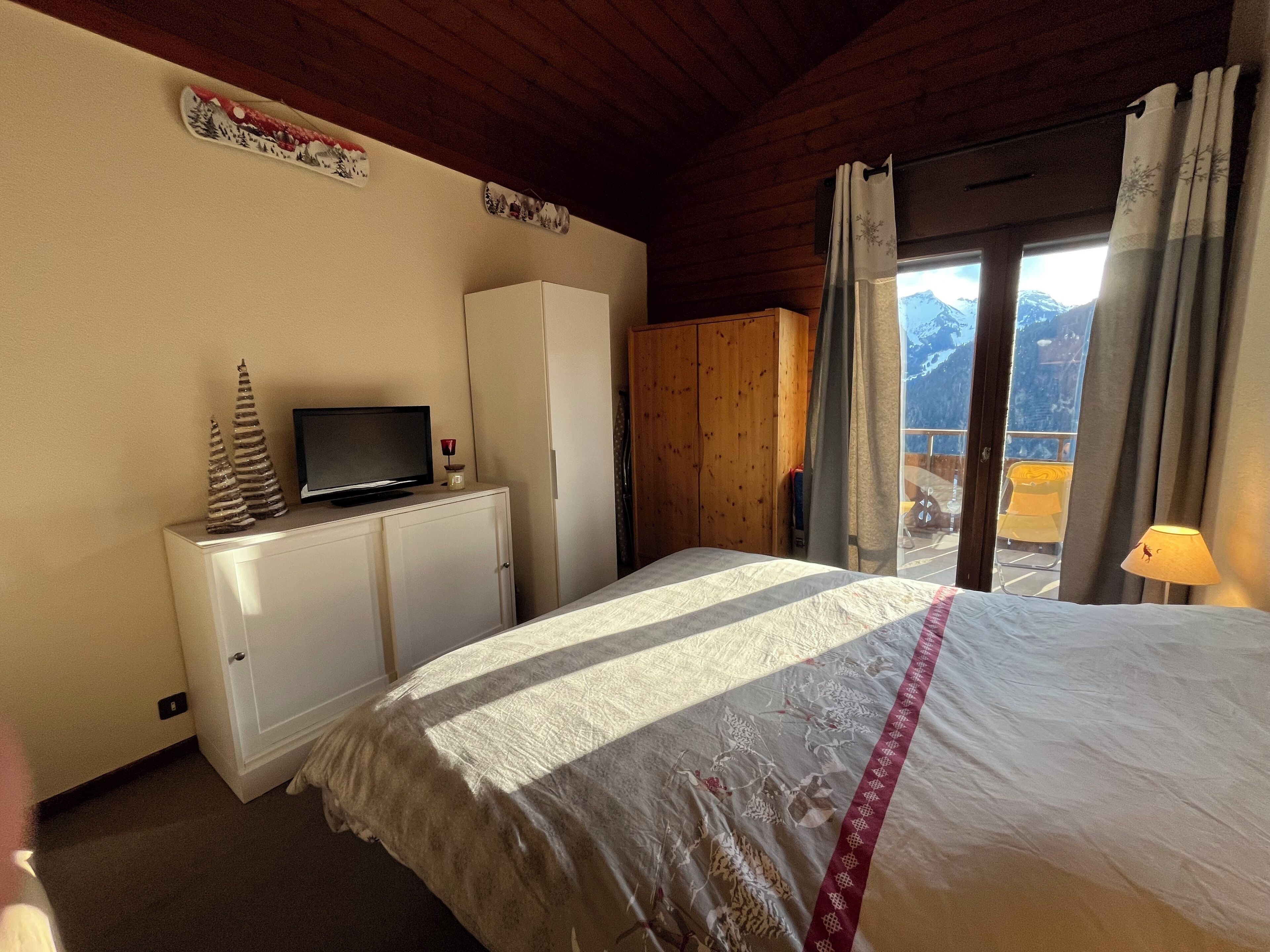 Ein Schlafzimmer mit einem Bett, einem Fernseher auf einem Schrank, einem Holzschrank und Blick auf Berge durch das Fenster.