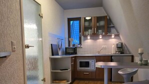 Eine kompakte Küche mit Mikrowelle, Herd und Schränken. Es gibt einen kleinen Essbereich mit Tisch und zwei Stühlen.