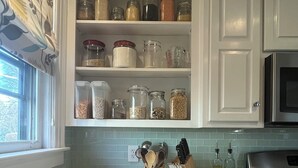 A kitchen with white cabinets, a window with a curtain, a fruit bowl, and various kitchen utensils on the counter. - Spacious 5-bedroom home with private yards - near Brown/RISD (Providence)
