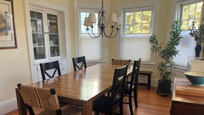 A dining room with a wooden table, six chairs, a chandelier, and a potted plant. - Spacious 5-bedroom home with private yards - near Brown/RISD (Providence)