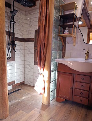 A bathroom with a shower, wooden cabinets, and a marble-tiled wall.