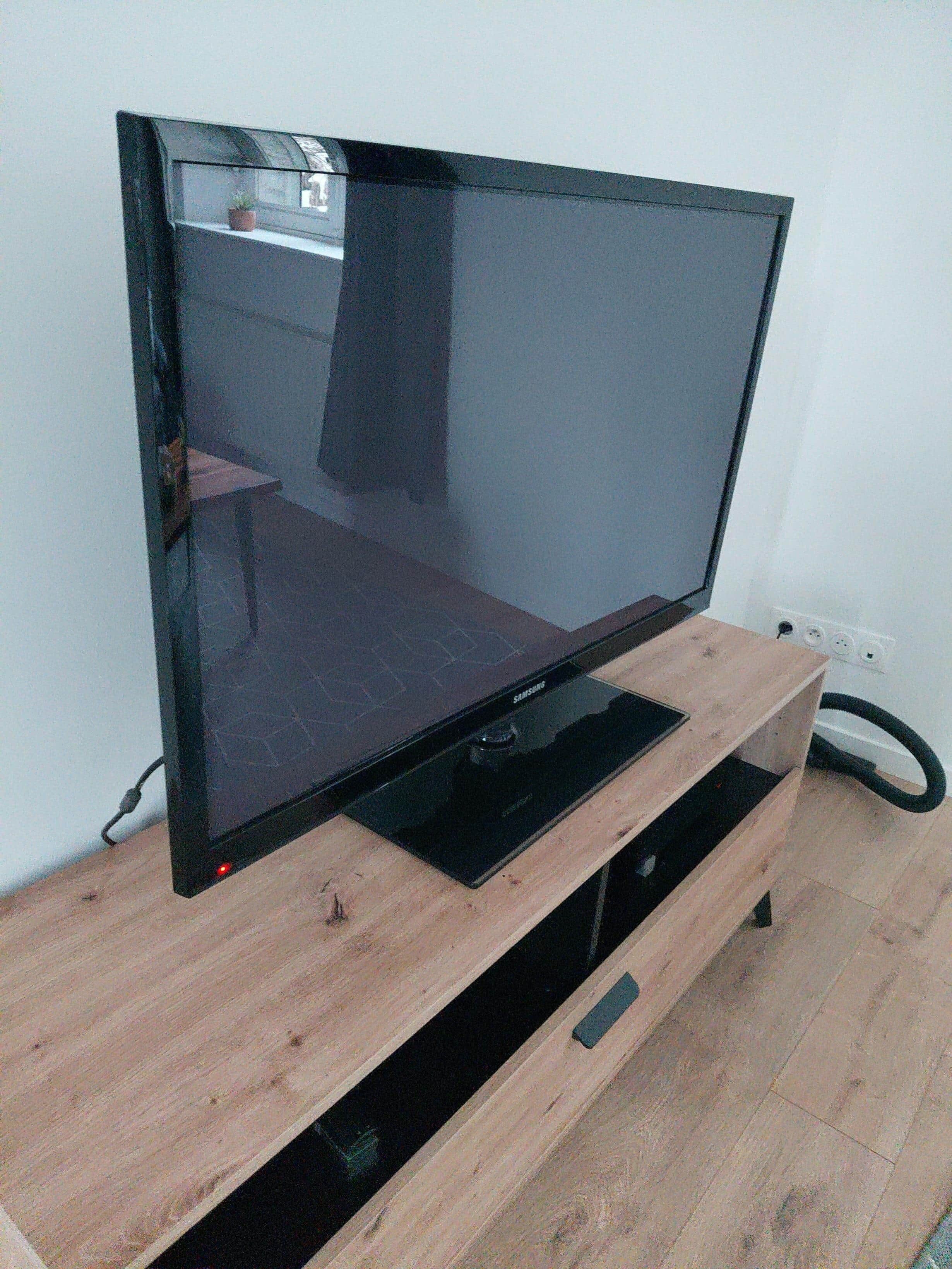 Een flatscreen-tv op een houten tv-meubel, met een aangesloten kabel.