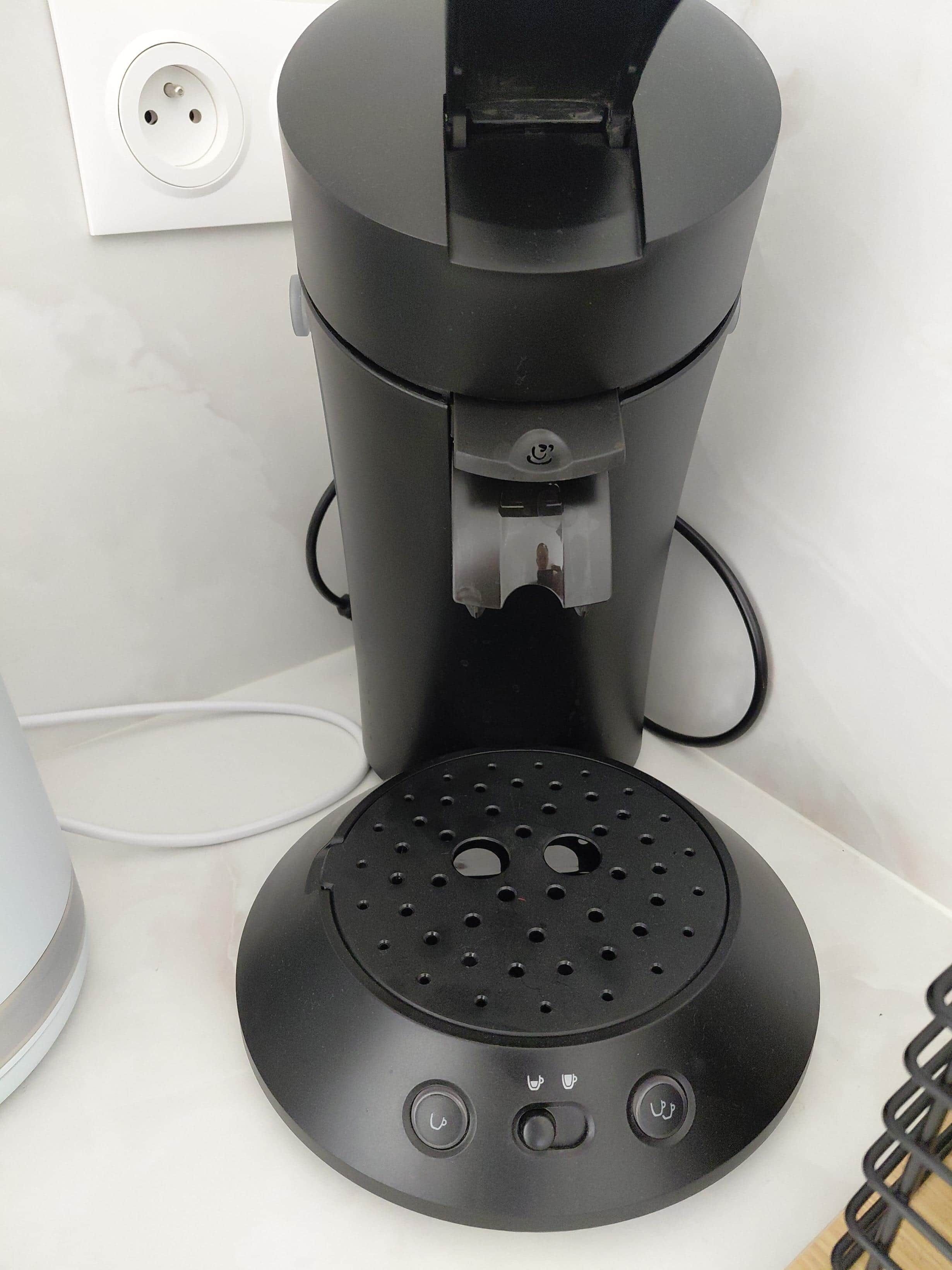 Une machine à café dotée d’un bac de récupération, d’un câble d’alimentation et d’une prise de courant murale.