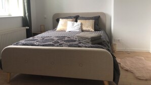 Un lit bien fait, avec une couvre-lit à motifs et des oreillers, un radiateur, une fenêtre avec des rideaux et une prise de courant sur le mur.