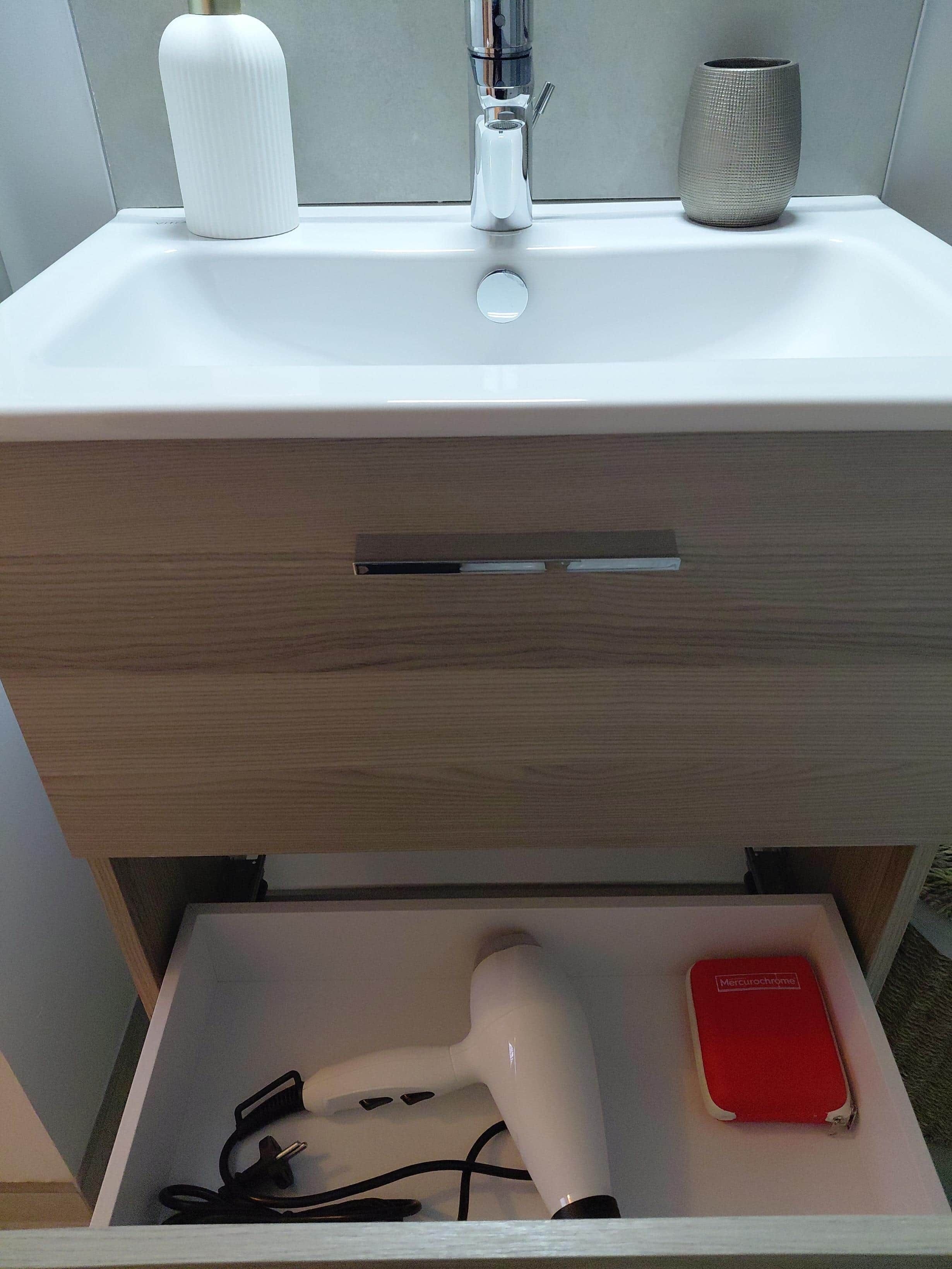 A bathroom with a white sink, a towel dispenser, and a hairdryer in a drawer.