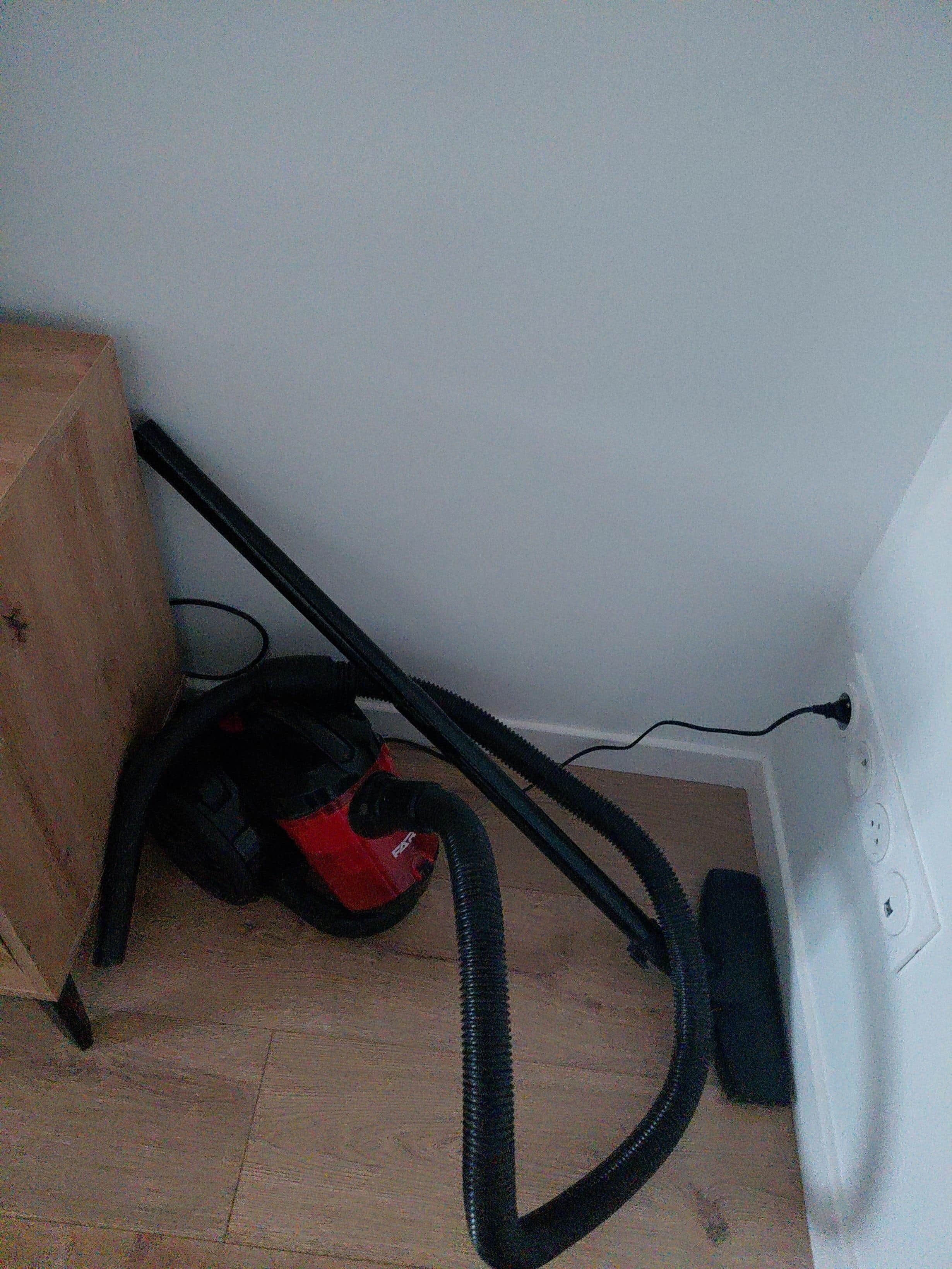 A vacuum cleaner in a room with a wooden floor and a white wall.