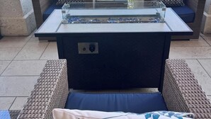 Zona de descanso junto a la piscina con mobiliario de mimbre y una mesa de vidrio, con vistas a una piscina y un complejo de edificios.