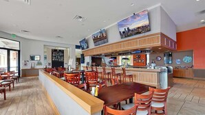 Un restaurante moderno con barra central, varias mesas para comer y un techo alto decorado con obras de arte.