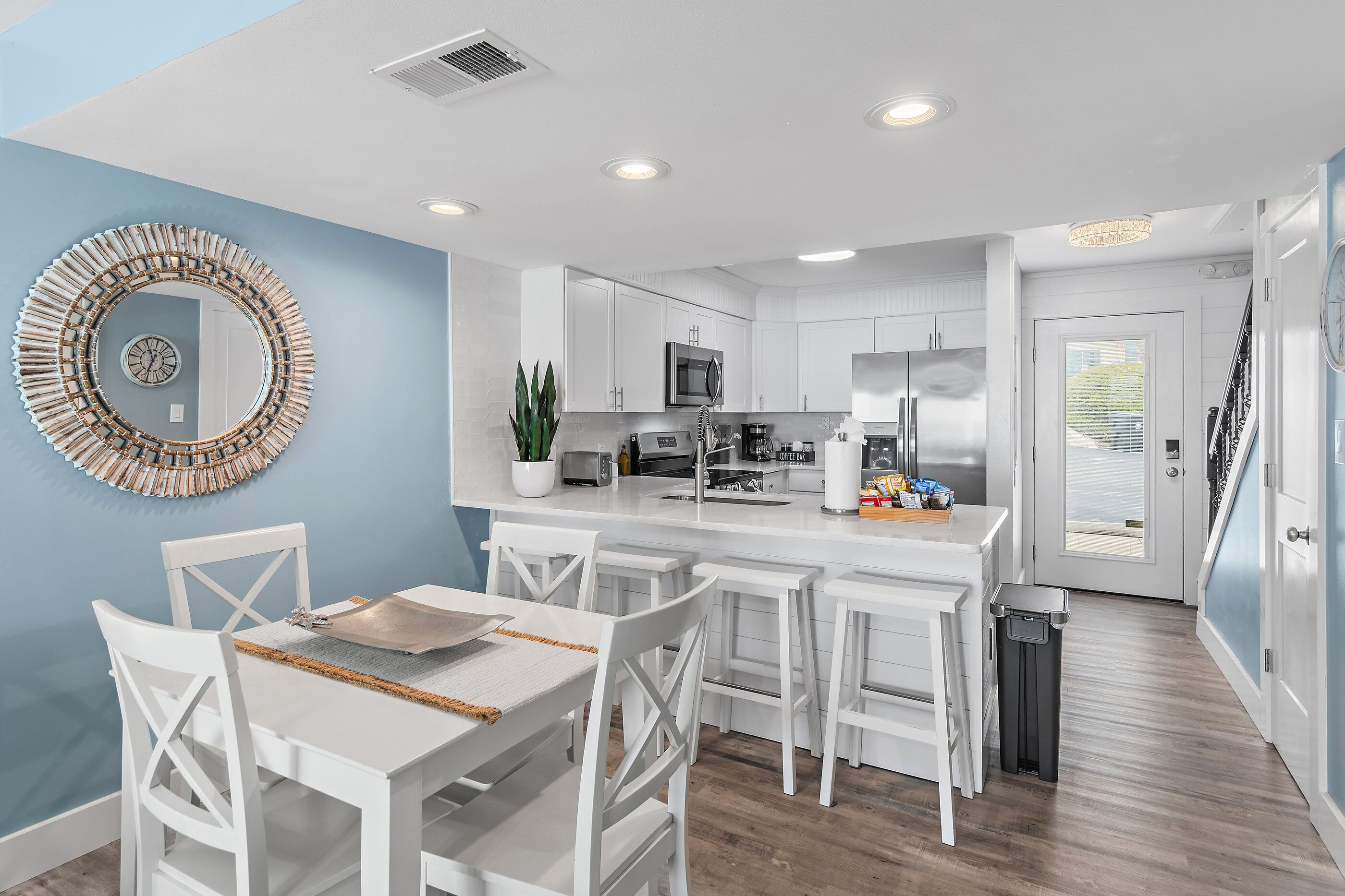 A modern kitchen with white cabinetry, a central island, and a dining area with white chairs.