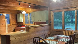 L’intérieur d’une cabane en bois comprend un coin repas, une cuisine et de grandes fenêtres.