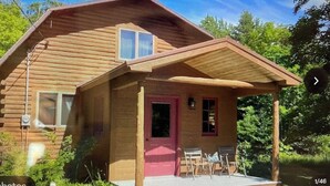 Une cabane en bois avec une véranda, une porte rouge et une petite fenêtre.