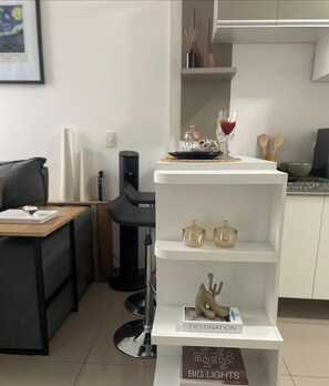 A modern kitchen with white cabinetry, a dining table with chairs, and a decorative shelf with a glass bottle and a candle. - LoftPrime Experience | Comfort • View & Sauna (São Bernardo do Campo)