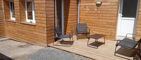 Une cabane en bois avec une terrasse, deux chaises et une table.