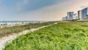 Una vista costiera con spiaggia, dune erbose e palazzi alti sullo sfondo.