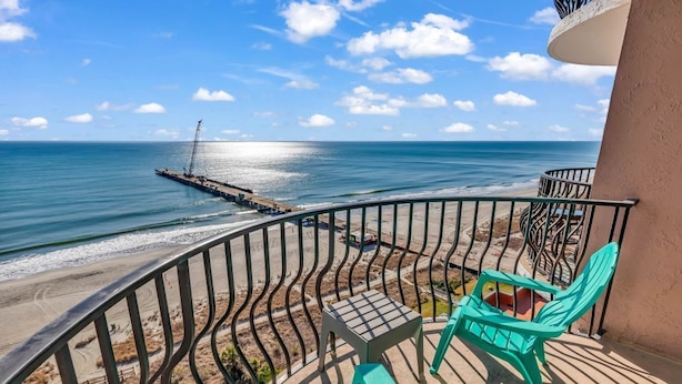 Un balcone con vista sulla spiaggia e sull'oceano, dotato di ringhiera, un tavolino e due sedie.