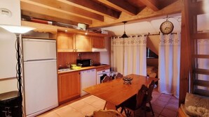 Une cuisine avec des meubles de rangement en bois, une table à manger, des chaises, un réfrigérateur et une horloge au mur.