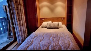 Une chambre avec une tête de lit en bois, un lit avec une literie blanche, une fenêtre avec des rideaux et une échelle en bois à l’extérieur.